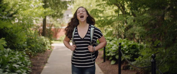 Student with a backpack on walking down a sidewalk on the mall, happily screaming with her mouth open.