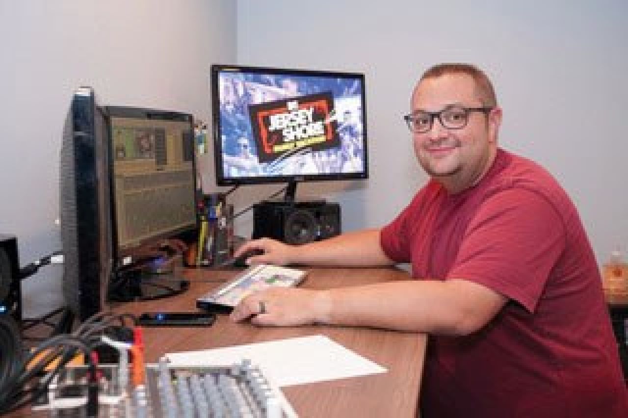 David Coppola poses in front of his computer with graphics from the TV show, The Jersey Shore, on screen.