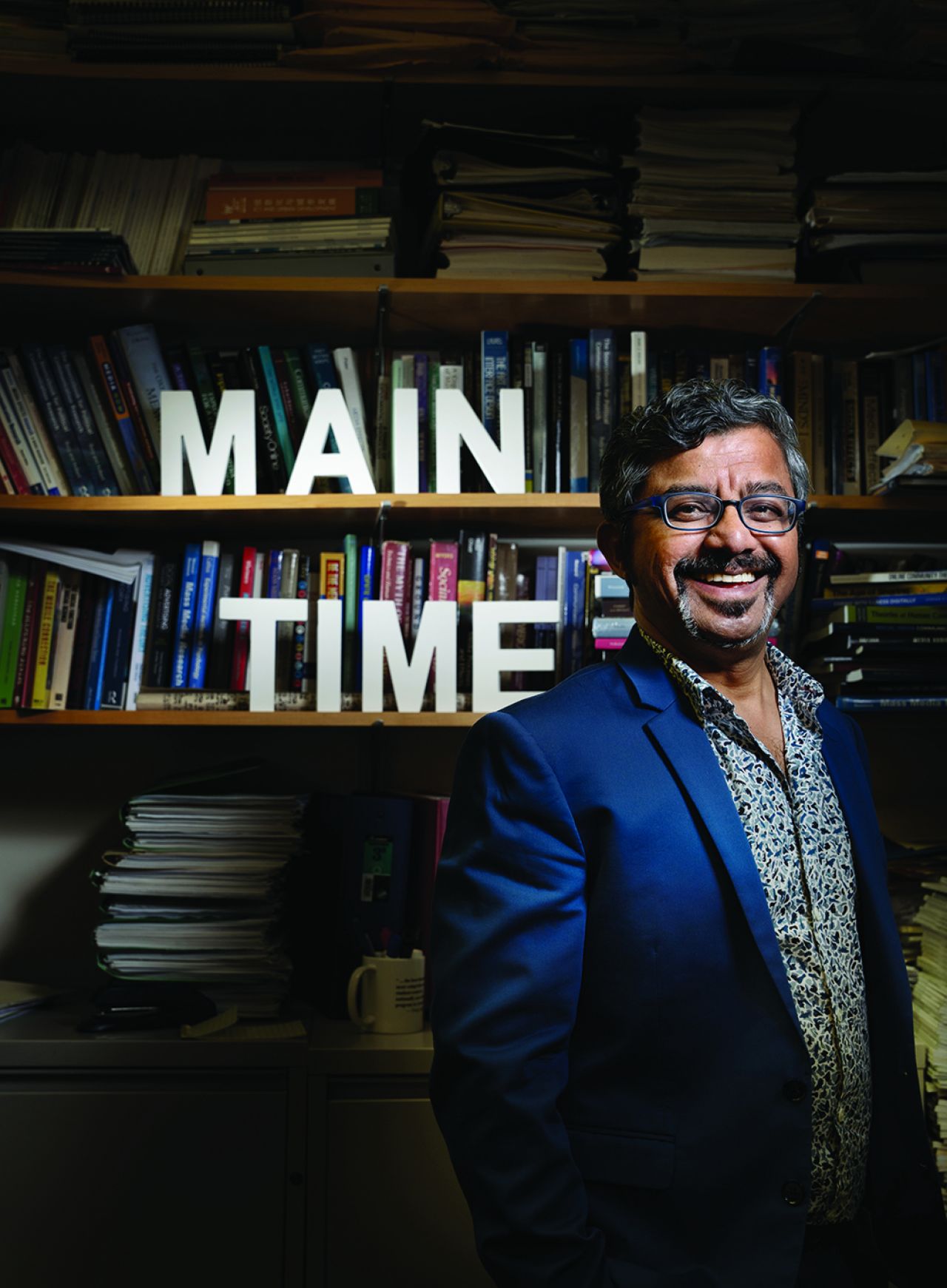 Dark haired man in mustache and glasses in blue sport coat