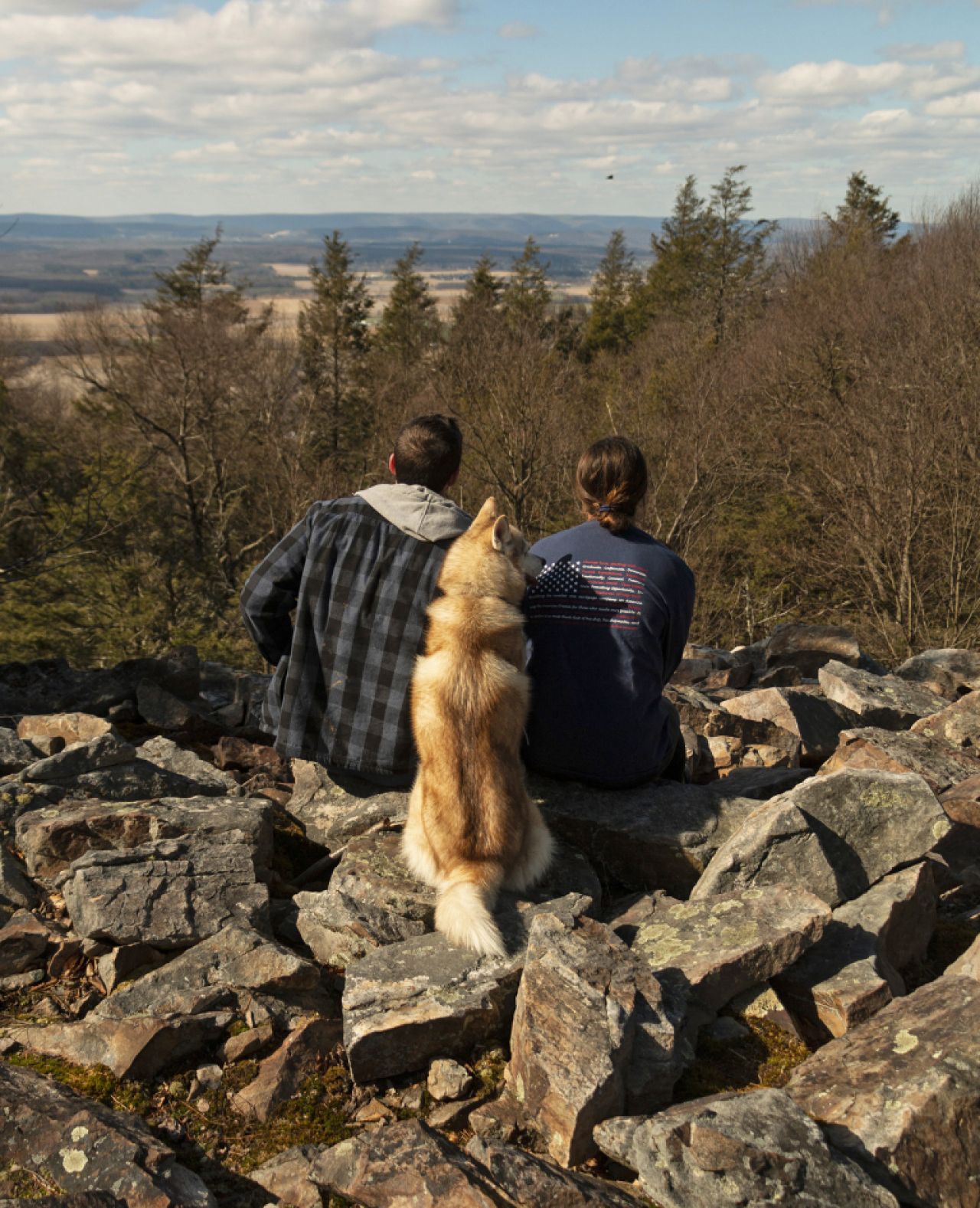 A couple sitting on a rock overlook with their dog