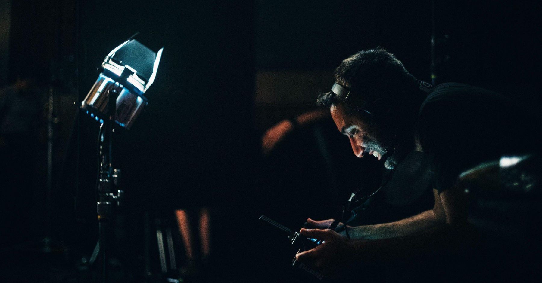 Moody shot on a dark set of Deepak Sethi wearing headphones and reviewing a shot on a camera