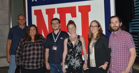 Six Penn State alumni members who work at NFL Films stand in front of a huge NFL logo