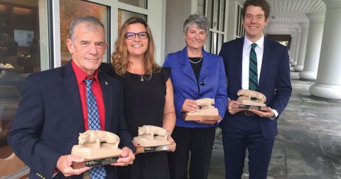 Four faculty, alumni, and industry members pose with Nittany Lion Shrine statuettes in front of the Hintz Family Alumni Center